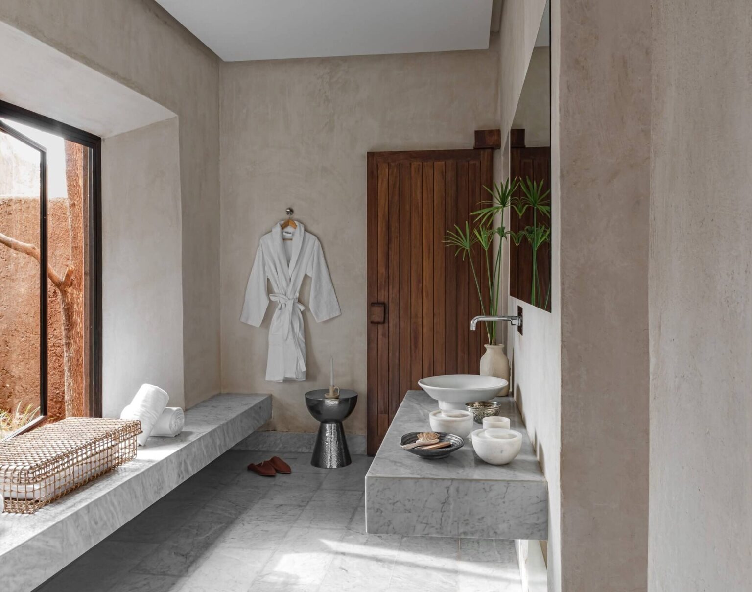 Relaxation room of a private spa in Marrakech: tadelakt walls, white marble bench and basins, bathrobe, rolled towels and babouche slippers on the floor