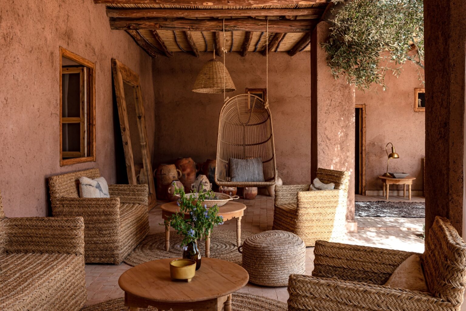 Terrasse couverte d'une maison marrakchie : murs en pisé, plafond de roseaux sur poutres de thuya, fauteuils en fibre de palmier, olivier et jarres anciennes