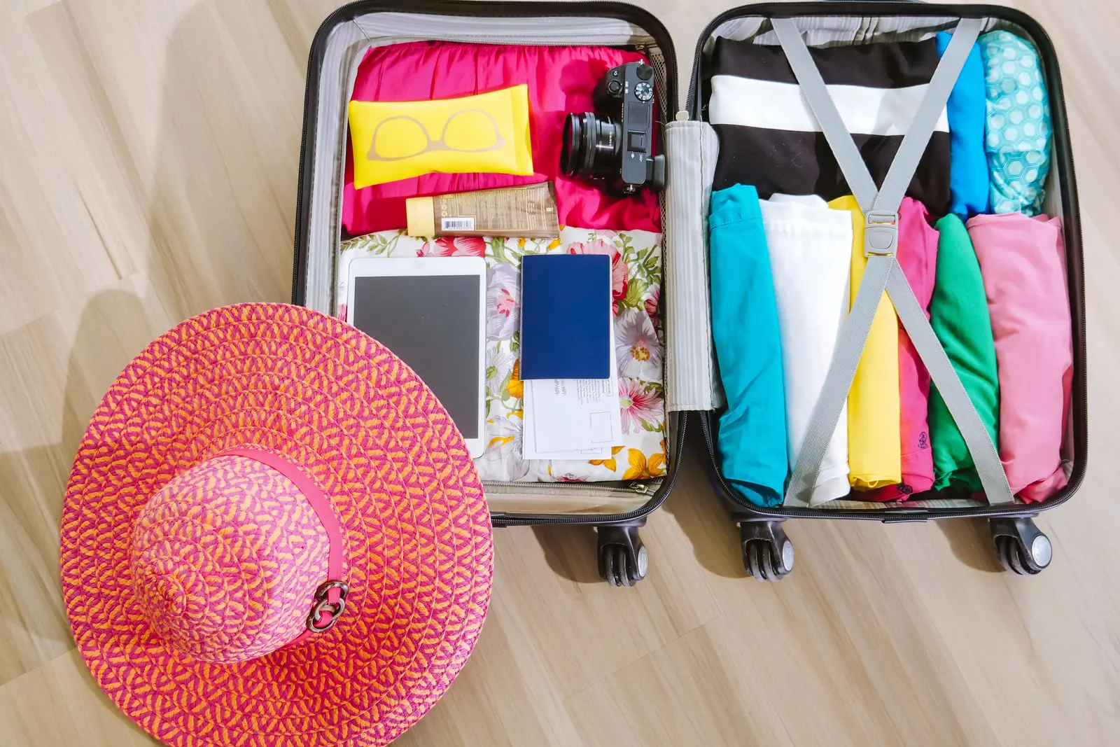 Open suitcase packed with clothes, a sun hat and a camera