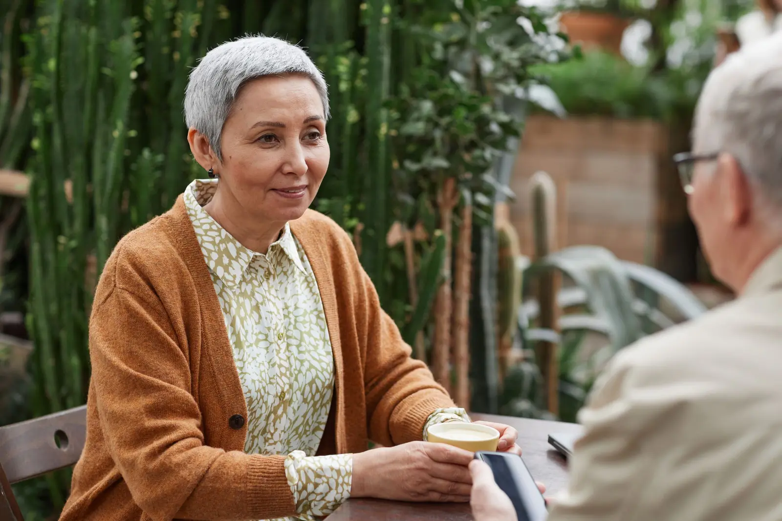 Senior couple chatting over coffee in a garden with cacti
