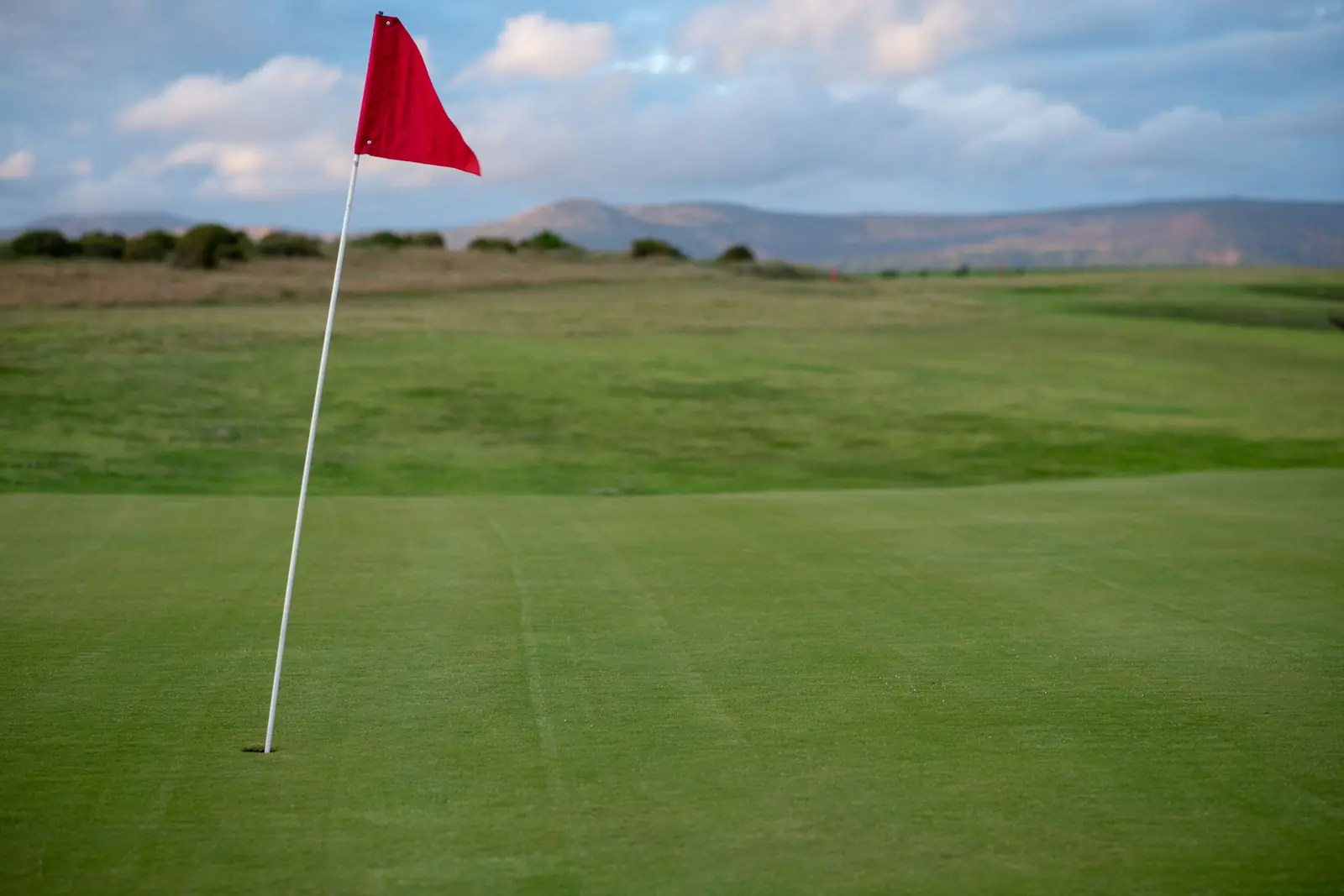 Red flag on a golf green with hills in the distance