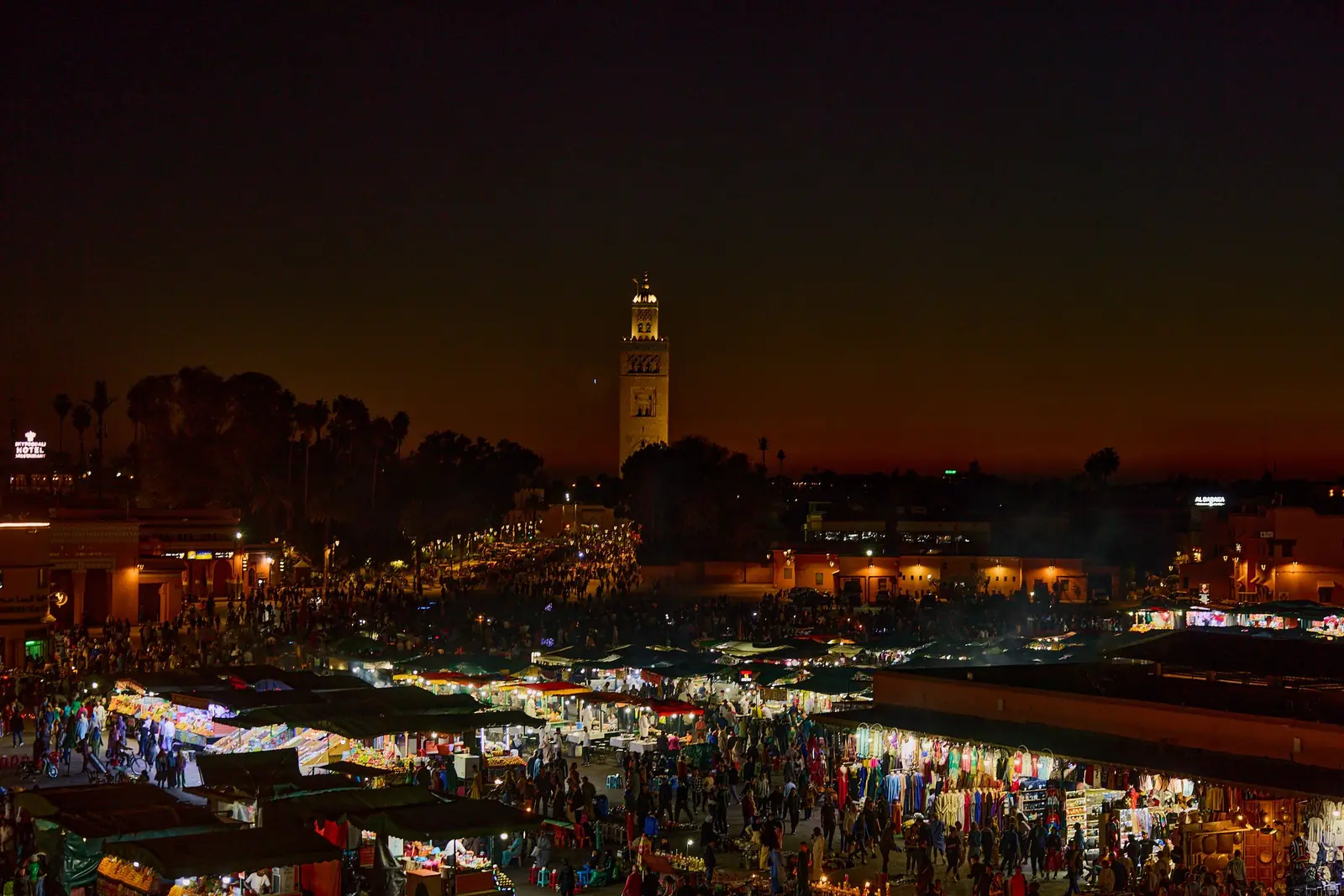 Jemaa el-Fna food stalls lit up at night, with the Koutoubia minaret behind