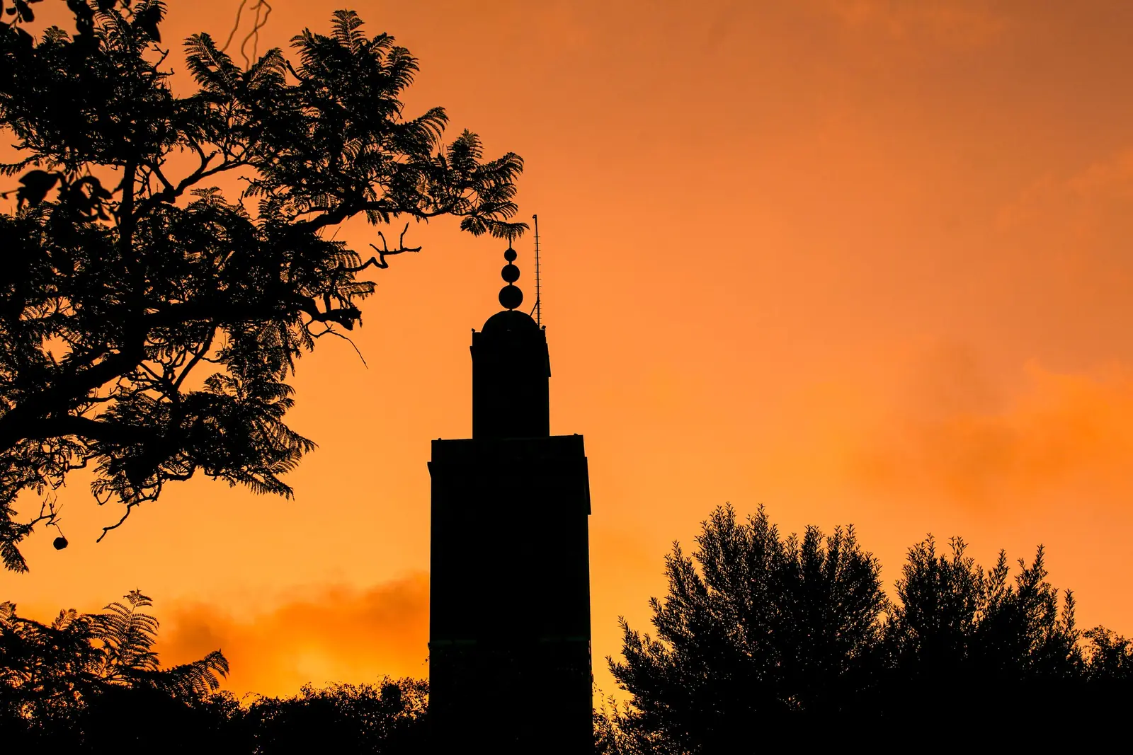 Minaret silhouetted against an orange sunset sky