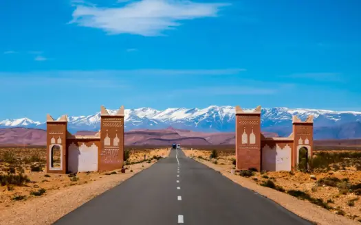 Road through a kasbah-style gate towards the snow-capped Atlas