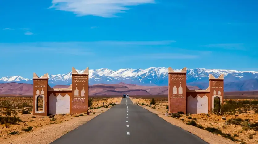 Road through a kasbah-style gate towards the snow-capped Atlas