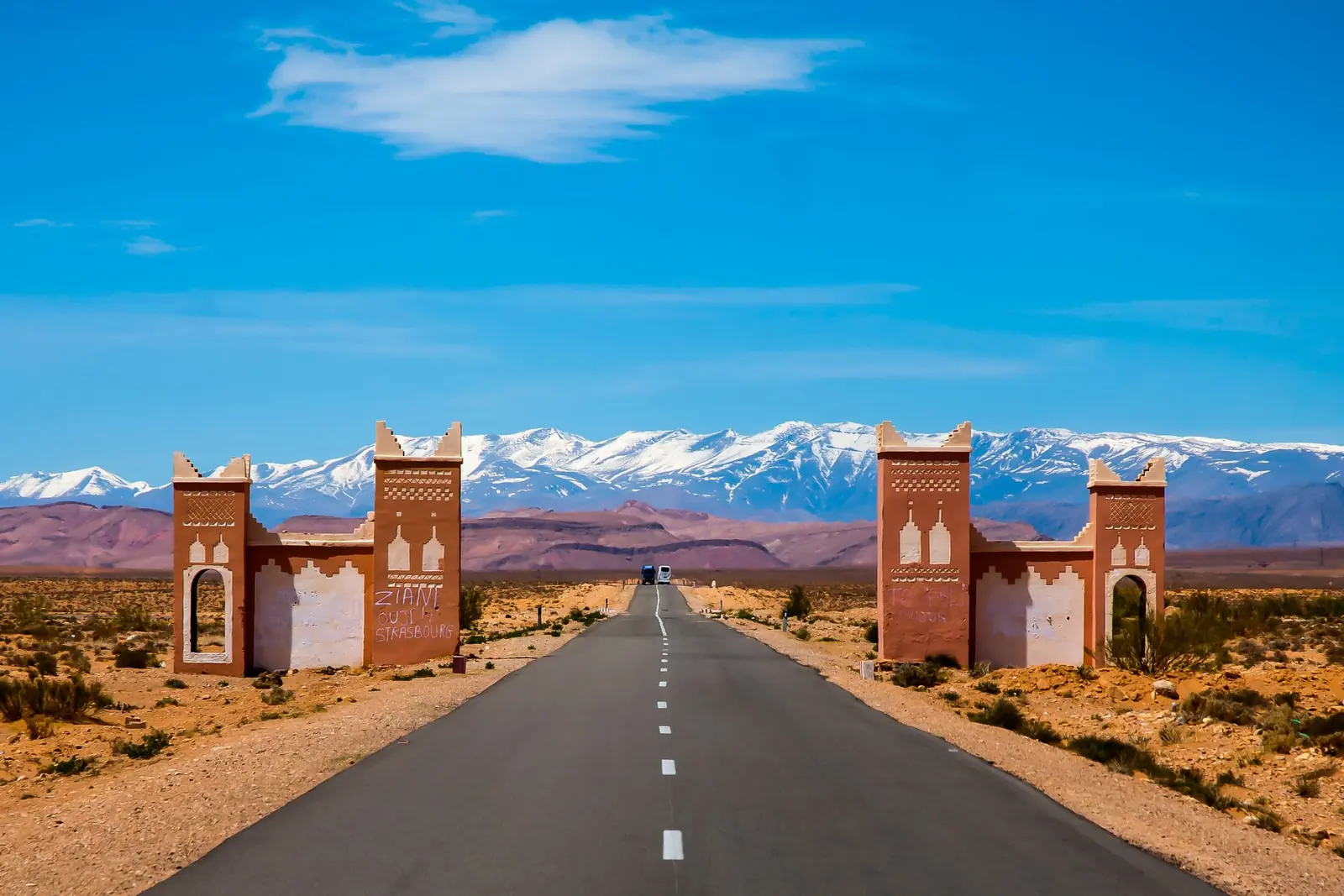 Road through a kasbah-style gate towards the snow-capped Atlas