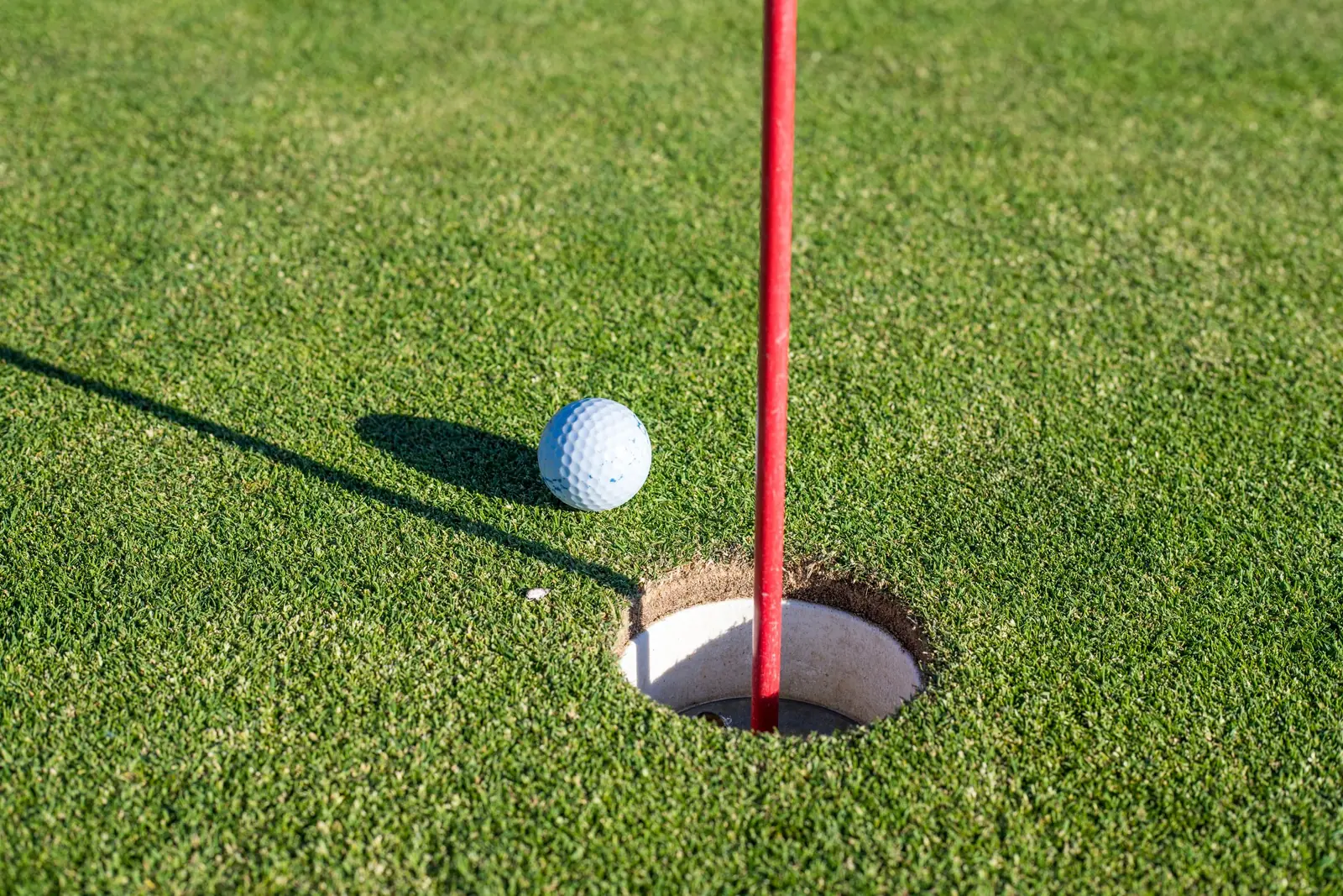 Golf ball on the edge of the hole, red flag on the green