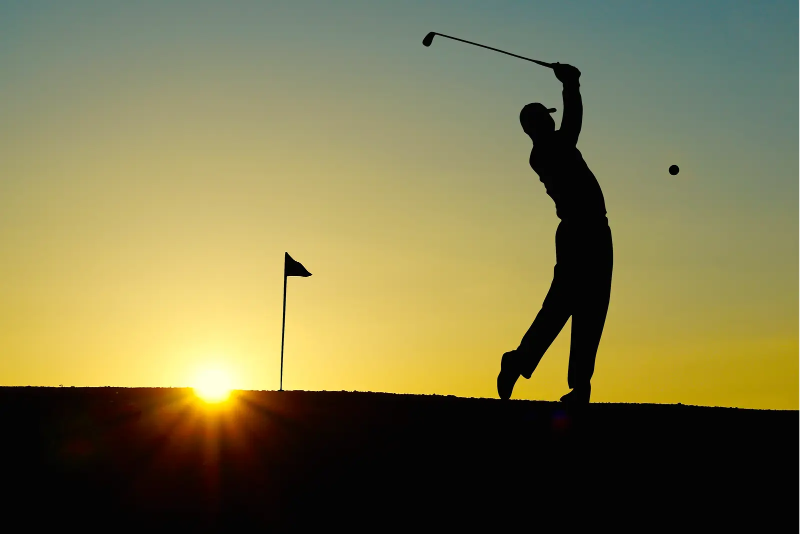 Golfer silhouetted against the sunrise mid-swing