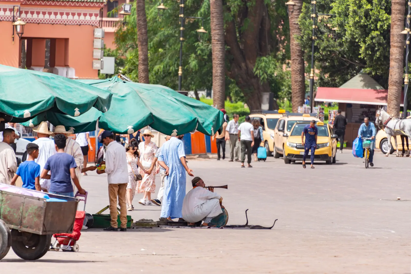 Stalls and pedestrians at the edge of Jemaa el-Fna, with beige petits taxis in the background