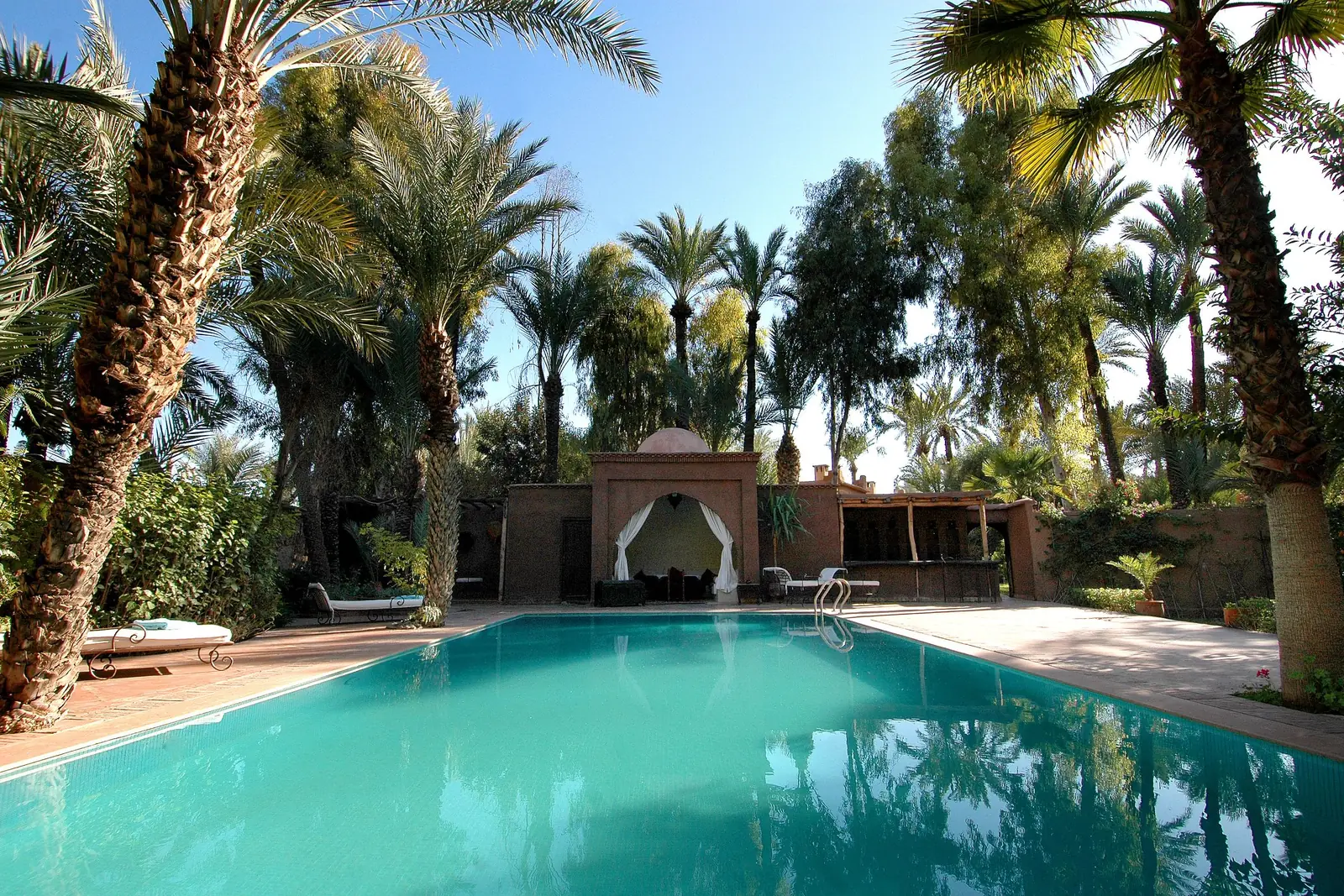 Piscine d'hôtel entourée de palmiers et d'un pavillon