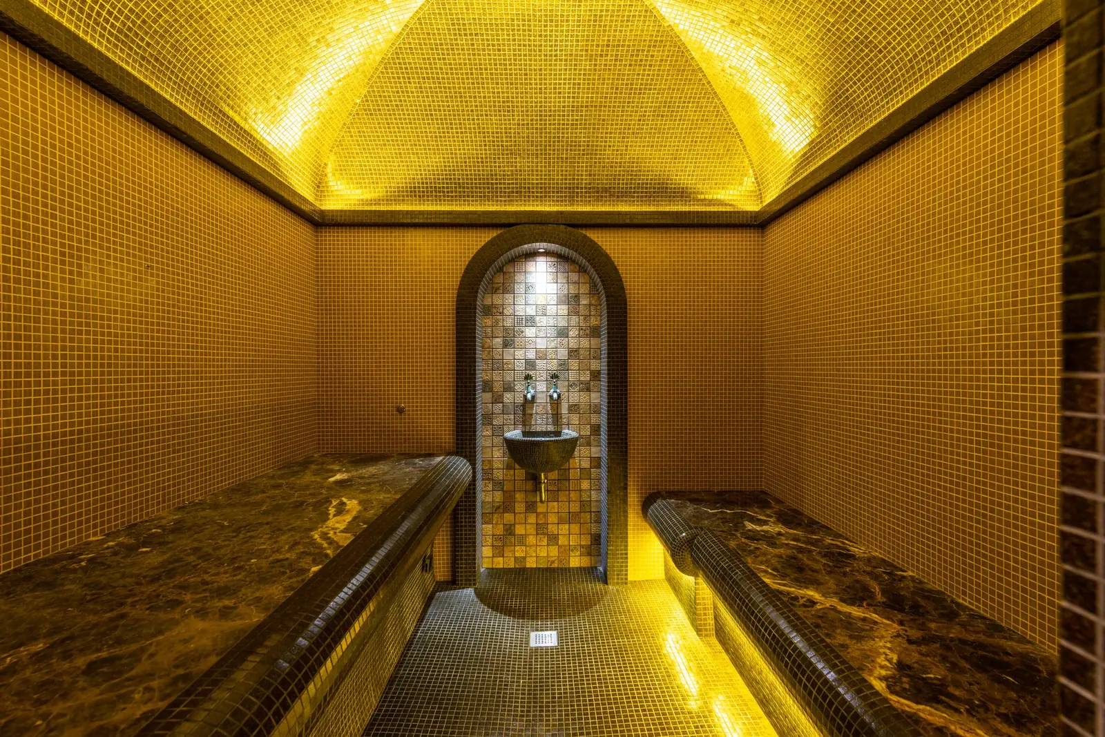 Tiled steam room of a hammam with marble benches and warm light