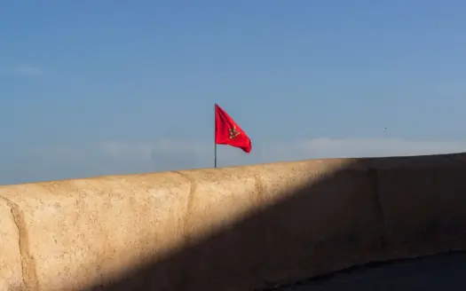 Moroccan flag flying above an ochre rampart under a clear sky