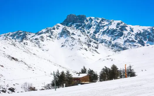 Snow-covered slopes, a ski-lift pylon and chalets below a High Atlas peak at Oukaimeden