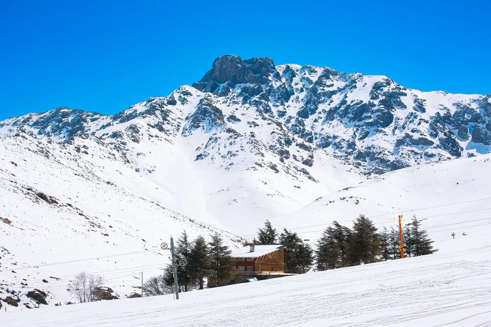 Snow-covered slopes, a ski-lift pylon and chalets below a High Atlas peak at Oukaimeden