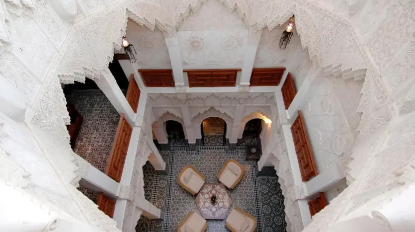 Courtyard of a traditional riad seen from the upper gallery, with carved plaster and a zellige floor