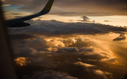 Sunlit clouds seen from an aircraft window, with the wing in view