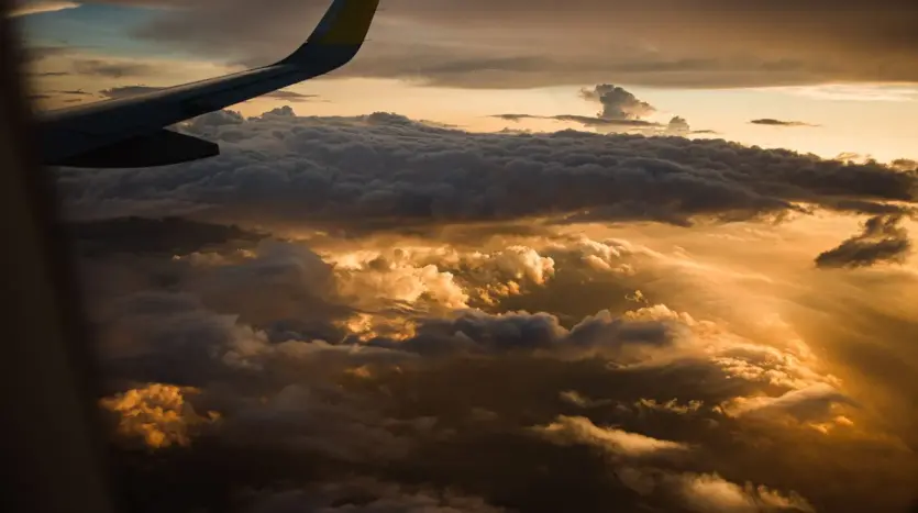 Sunlit clouds seen from an aircraft window, with the wing in view