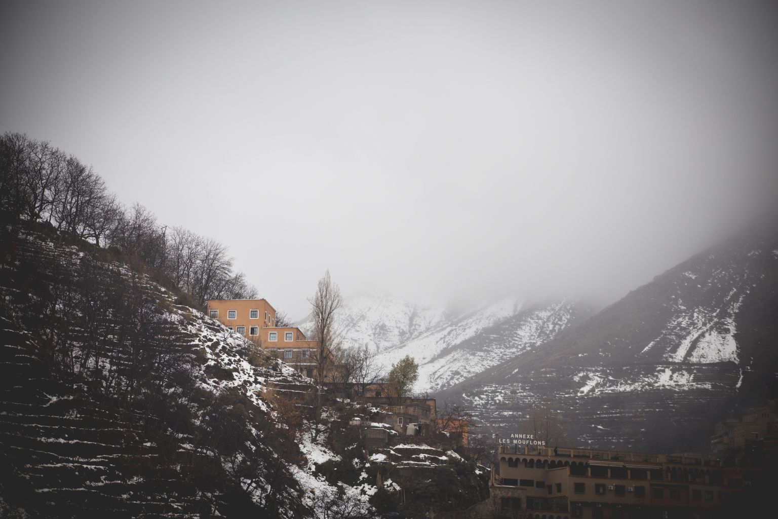 Snow on the terraced slopes above Imlil in the High Atlas, ochre village houses under a low winter mist