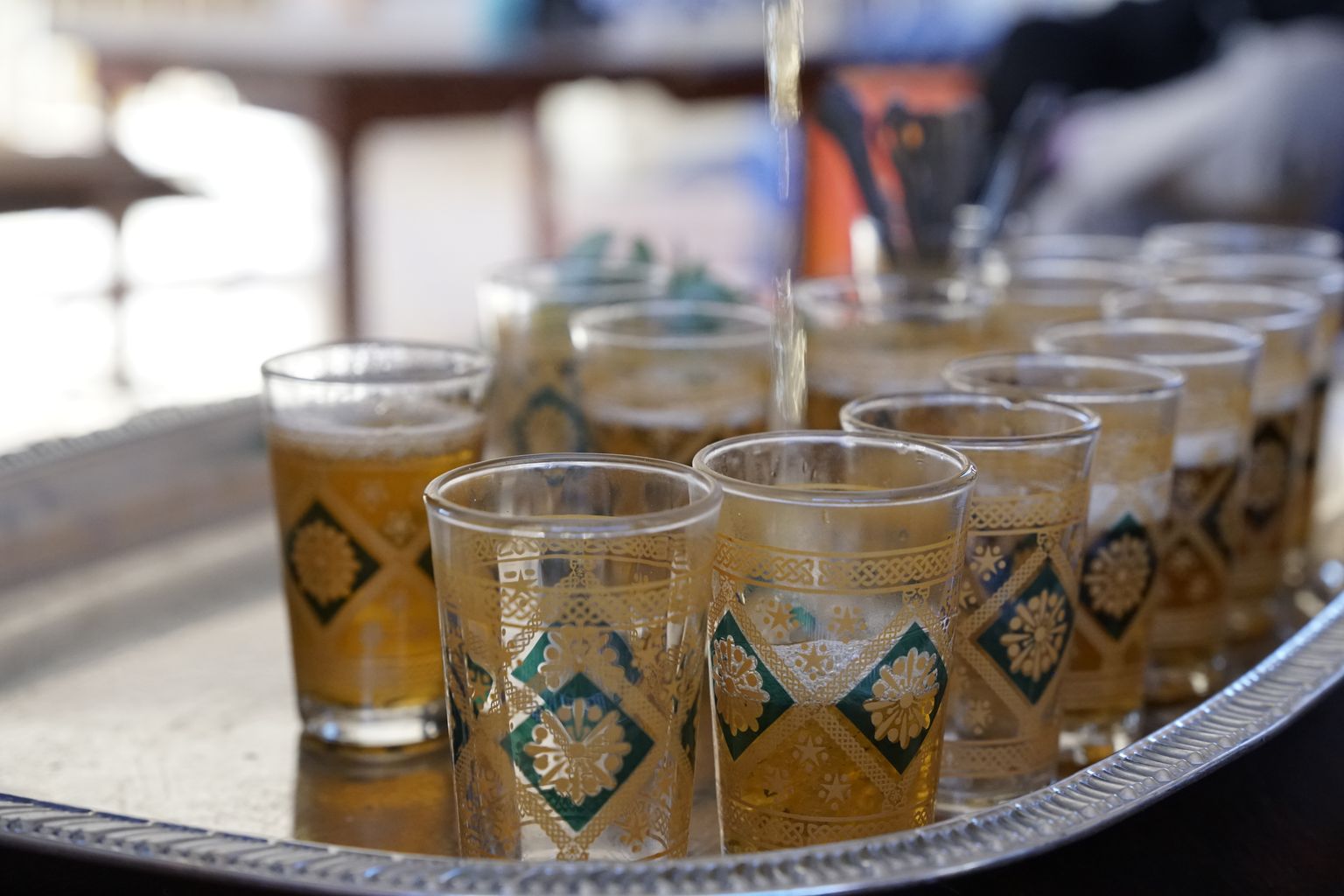 Gilded Moroccan tea glasses on an engraved silver tray as mint tea is poured