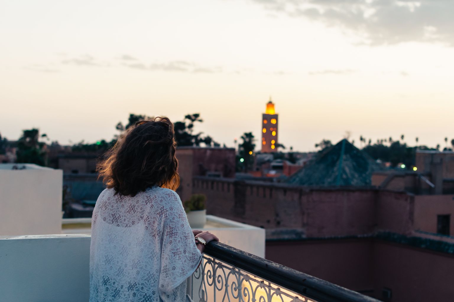 Vue depuis une terrasse rooftop de Marrakech au coucher du soleil, avec le minaret illuminé de la Koutoubia