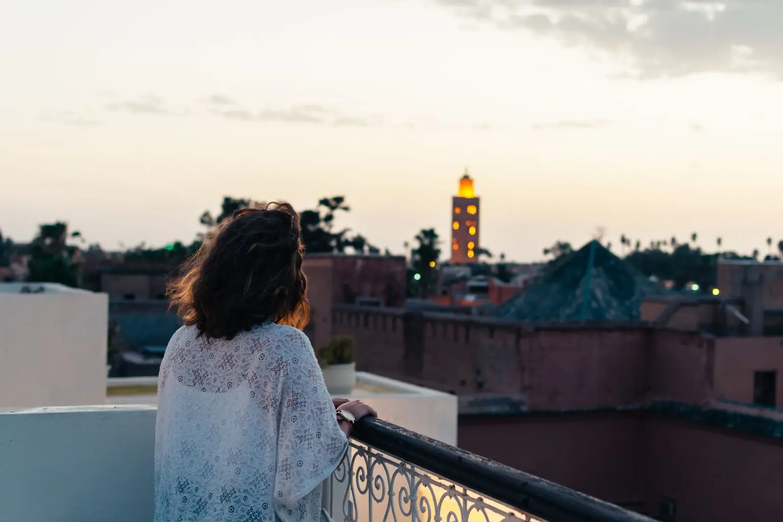 Vue depuis une terrasse rooftop de Marrakech au coucher du soleil, avec le minaret illuminé de la Koutoubia à l'horizon